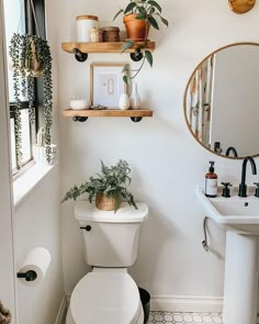 a white toilet sitting under a bathroom mirror next to a sink and a potted plant