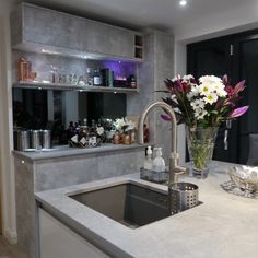 a kitchen with a sink, counter top and shelves filled with bottles on the wall