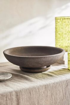 a wooden bowl sitting on top of a table next to a green vase and money