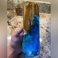 a hand holding a glass bottle with blue and green liquid in it on top of a counter