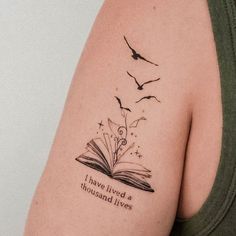 a woman's arm with a book and birds tattoo on it that says i have lived a thousand lives