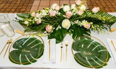 the table is set with white and green plates, silverware, flowers and greenery