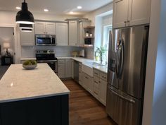 a large kitchen with white cabinets and stainless steel appliances, along with an island in the middle