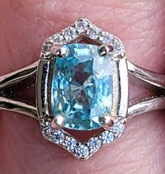 a woman's hand holding a ring with an aqua blue stone and diamond accents