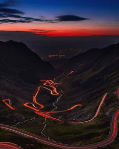 an aerial view of a winding mountain road at night with red lights on the roads