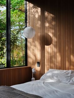 a bed with white sheets and pillows in a bedroom next to large windows that look out onto the jungle