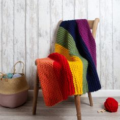 a multicolored blanket sitting on top of a wooden chair next to a ball of yarn