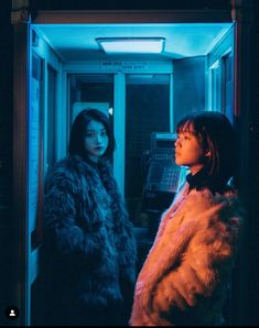 two women standing next to each other in front of a phone booth with blue lights