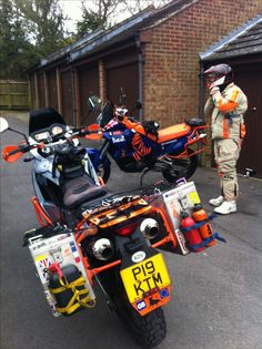 an orange and black motorcycle parked in front of a brick building with two men standing next to it