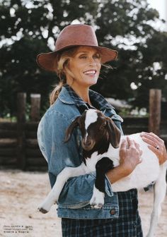 a woman wearing a cowboy hat holding a small dog in her arms and smiling at the camera