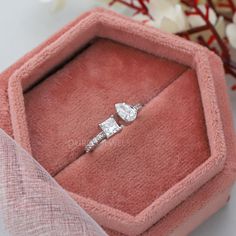 an open pink velvet ring box with two diamond rings in it and some flowers on the side