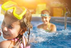 two children in a swimming pool with goggles on their head and one child smiling at the camera