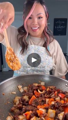 a woman holding a wooden spoon over a pan filled with food