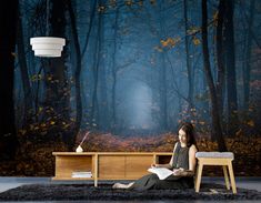 a woman is sitting on the floor in front of a table with books and a lamp