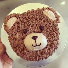 a teddy bear cake with chocolate frosting on top is being held by a person's hand