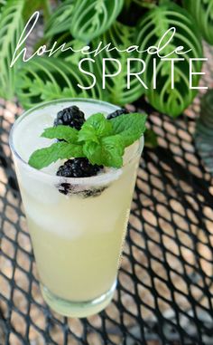 a glass filled with lemonade and blackberries on top of a table next to plants