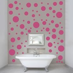 a bath tub sitting under a mirror next to a wall with pink and gold dots on it