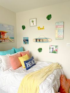 a white bed topped with lots of pillows next to a wall covered in pictures and paintings