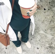 a woman holding a cup of coffee in her hand and wearing green pants with white shoes