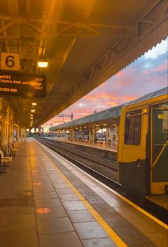 a yellow and black train pulling into the station at sunset or dawn with people sitting on benches next to it