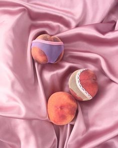 two peaches sitting on top of a pink satin