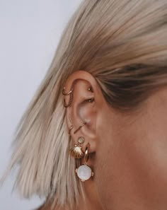 a woman with blonde hair wearing gold ear cuffs and an earring that has a shell on it