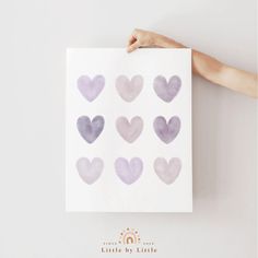 a person holding up a paper with purple hearts on it in front of a white wall