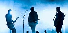 the silhouettes of four people on stage with guitars and microphones in front of them