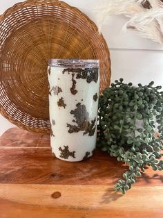 a glass with white and brown designs sitting on a wooden table next to a plant