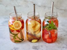 three mason jars filled with different types of fruit and veggies, sitting on a marble surface