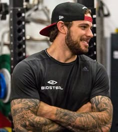 a man with his arms crossed standing in front of a gym equipment rack and looking off to the side