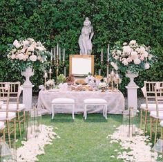 a table with white flowers and candles on it in front of a wall full of greenery