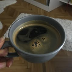 a person holding a cup of coffee in their hand on a wooden floor next to a rug