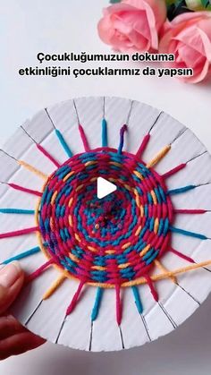 a person is holding a paper plate with yarn on it and flowers in the background