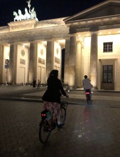 a person riding a bike in front of a building with columns and lights at night