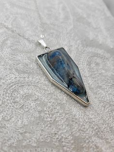 This beautiful handmade, one-of-a-kind silver pendant with a real Blue Apatite Stone accent is perfect for dressing up or down. This pendant has approximately a height of 2 in. x 1 in. in length and is made from a durable silver metal alloy, and stone set in blue mica tinted resin. Blue Teardrop Pendant Jewelry With Large Stone, Blue Labradorite Jewelry With Large Stone, Silver Kyanite Jewelry As Gift, Silver Kyanite Jewelry For Gift, Unique Blue Sterling Silver Jewelry, Unique Blue Rectangular Pendant Jewelry, Blue Sterling Silver Amulet Jewelry, Nickel-free Blue Labradorite Jewelry, Unique Blue Jewelry With Large Pendant