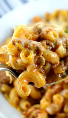 a spoon full of macaroni and cheese on a white plate with some meat