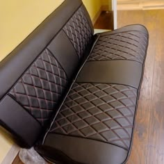 a black leather seat with diamond stitching on the back and armrests is sitting on a wood floor