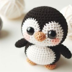 a small crocheted penguin sitting on top of a white table next to balls of yarn