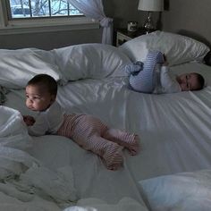 two babies laying on top of a bed covered in white sheets