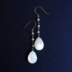 Long earrings made of white pearl and pearl - Perrine Perrine 【 Korintohs 】 This series of shell necklaces and earrings features beautiful Corinthian acanthus plant patterns inspired by the decorations of Greek temples. Light-reflecting white stones and black shadows, elegant decoration and rational structure, magnificent construction and a design that embraces light and wind. The characteristics of ancient Greek temples have been sublimated into summer jewelry. These long earrings are made from chains carefully spun from the smallest, most precious freshwater pearls on the market, which are difficult to cultivate, and feature white mother of pearl at the ends, giving them a delicate and elegant charm. The design, which resembles a single drop of water on the surface of the water, gives a Handmade White Mother Of Pearl Earrings, Dainty Mother Of Pearl Jewelry For Wedding, Pearl White Drop Earrings Made Of Mother Of Pearl, Pearl White Drop Earrings In Mother Of Pearl, Handmade White Earrings In Mother Of Pearl, Delicate Mother Of Pearl Jewelry In Pearl White, Pearl White Mother Of Pearl Jewelry As A Gift, Pearl White Mother Of Pearl Jewelry For Gift, Elegant Mother Of Pearl Earrings As Gift