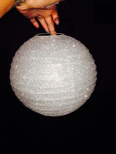 a person holding onto a large white ball ornament in the dark with their hand