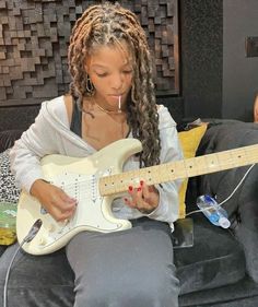 a woman sitting on a couch with a white guitar in her lap and looking at it