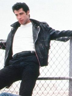 a man in black jacket and white shirt riding a skateboard next to a fence