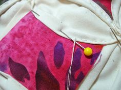 a piece of fabric with a yellow pin on it sitting next to some sewing needles