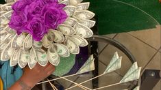 a person holding a bouquet of flowers made out of dollar bills on a bike wheel