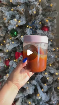 a person holding a cup with liquid in front of a christmas tree