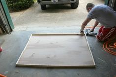 a man working on an unfinished piece of plywood in front of a garage door