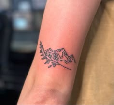 a small tattoo on the arm of a woman with mountains and leaves in the background