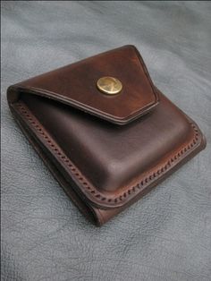 a brown leather wallet sitting on top of a gray surface with a gold button in the center